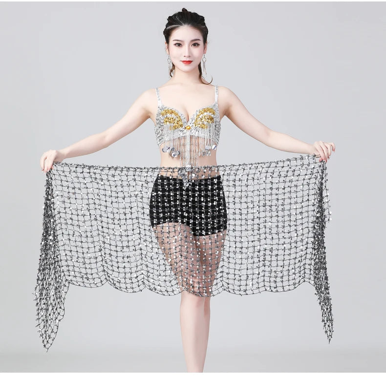 Woman wearing a beaded belly dance costume with decorative shawl and black shorts on a plain background
