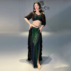 Woman wearing a green sequin crop top and skirt set with black ruffled overlay, posing indoors.