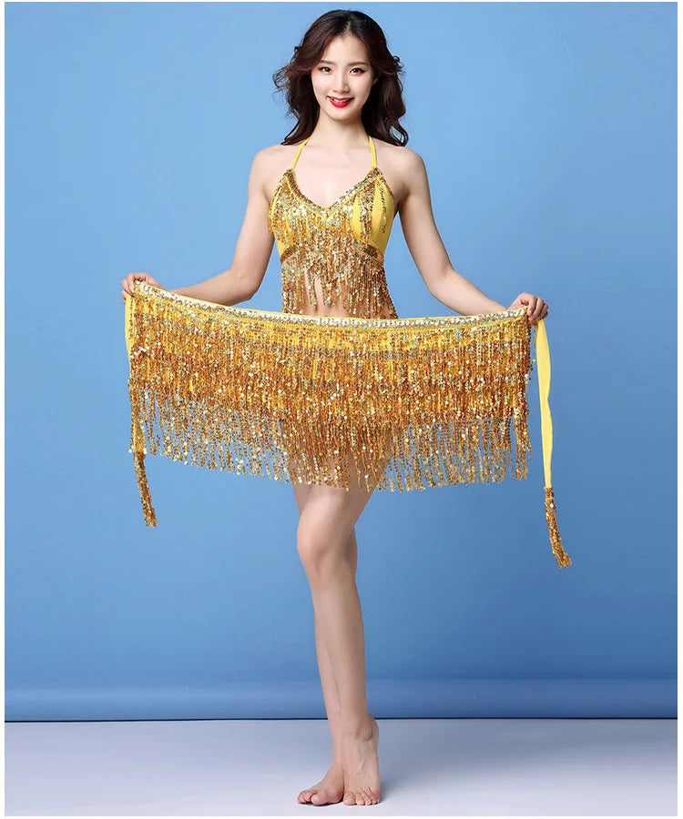 Woman in sparkly yellow fringe dance outfit posing barefoot against blue background