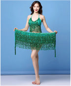 Woman in green sequin belly dance costume with tasseled skirt against blue background
