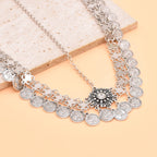 Silver coin necklace with ornate floral pendant on a beige stone background