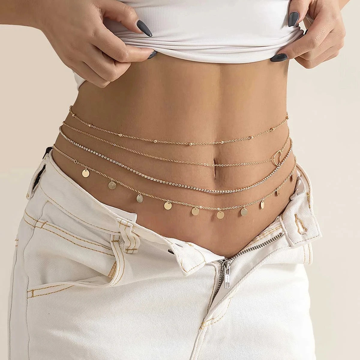Layered gold waist chain jewelry on woman's bare waist with white denim jeans