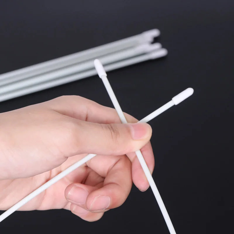 Hand holding white cotton swabs with rounded tips on black background, cleaning tools