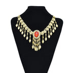 Gold statement necklace with red gemstone and dangling teardrop charms on black display