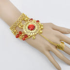 Gold hand chain bracelet with red gemstone centerpiece and beaded accents on mannequin hand
