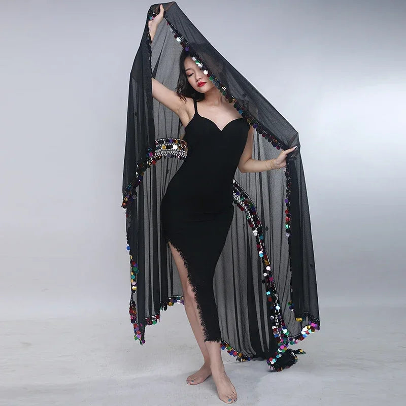Woman in black dress with sheer black shawl adorned with colorful pompom trim, posing indoors.