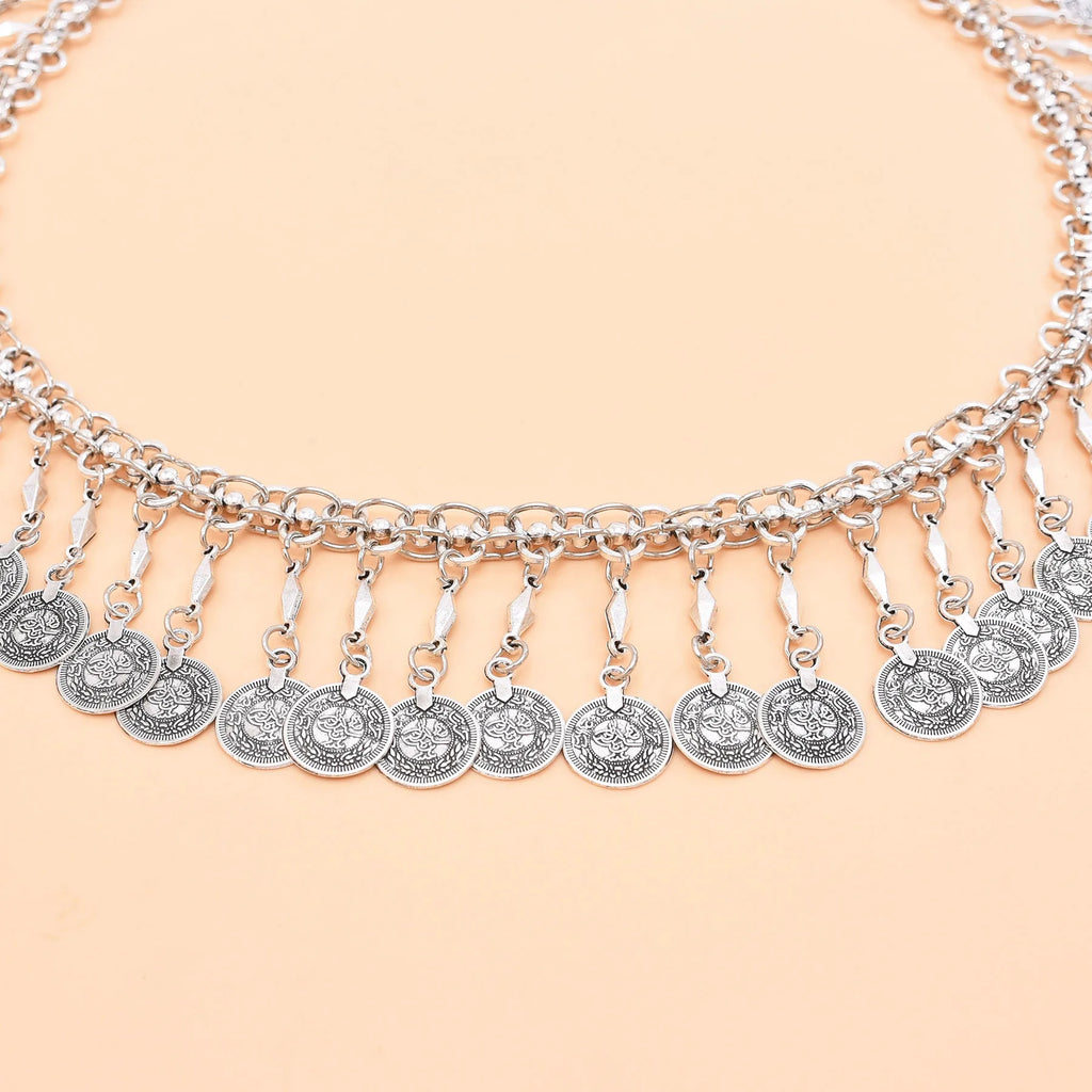 Silver coin charm necklace with intricate detailing on a peach background