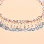 Silver coin charm necklace with intricate detailing on a peach background