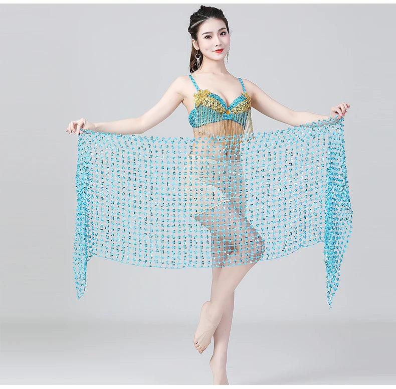 Woman modeling a blue and gold belly dance costume with sheer beaded scarf, standing on one foot.