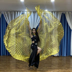 Woman performing dance with gold metallic wings in black dress, indoor setting with curtains