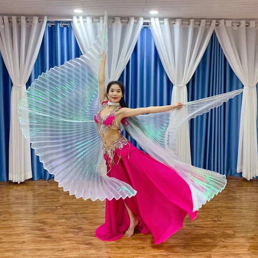 Woman in bright pink belly dance costume with iridescent wings posing on wood floor indoors