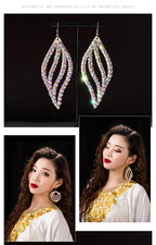 Woman wearing large, sparkly crystal dangle earrings with wave design, elegant outfit