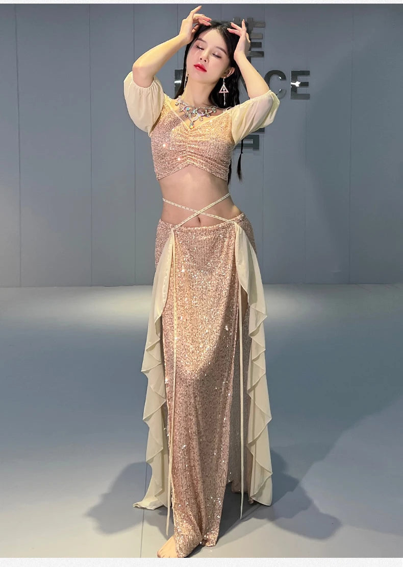 Woman in sequin belly dance costume with sheer sleeves and layered skirt panels indoors
