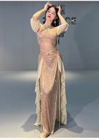Woman in sequin belly dance costume with sheer sleeves and layered skirt panels indoors