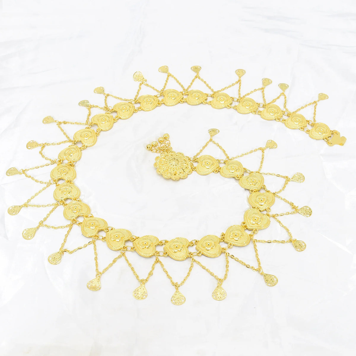 Gold waist chain with floral motifs and dangling tear-shaped charms on white background