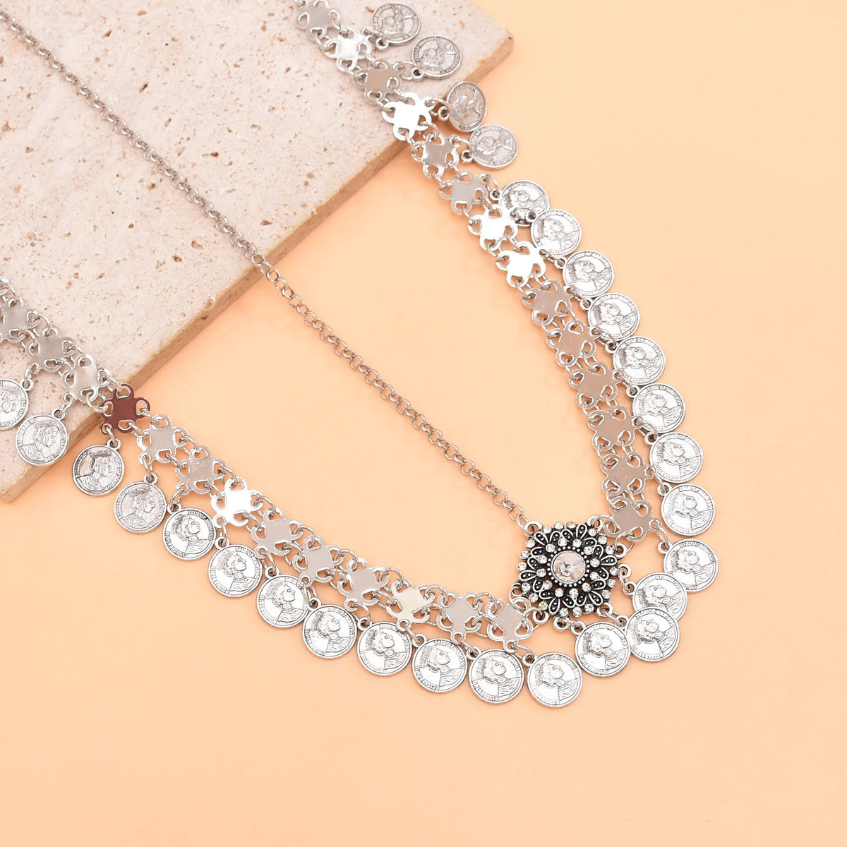 Silver coin statement necklace with intricate pendant on peach and stone background