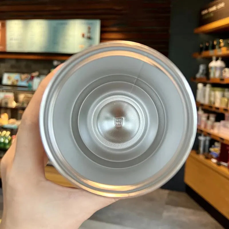 Hand holding stainless steel tumbler cup in a modern café setting