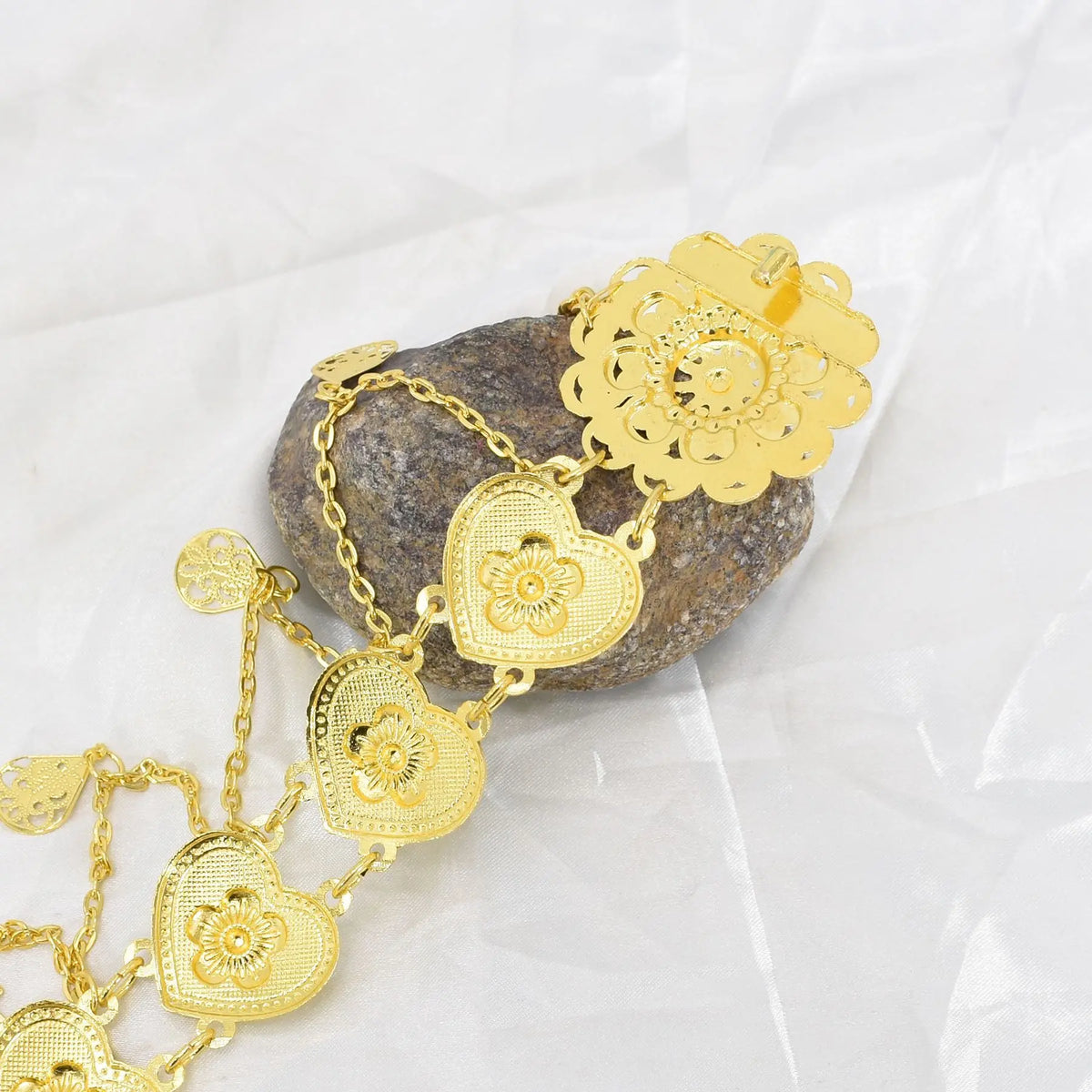 Gold heart chain bracelet with floral details on a stone, displayed on white fabric.
