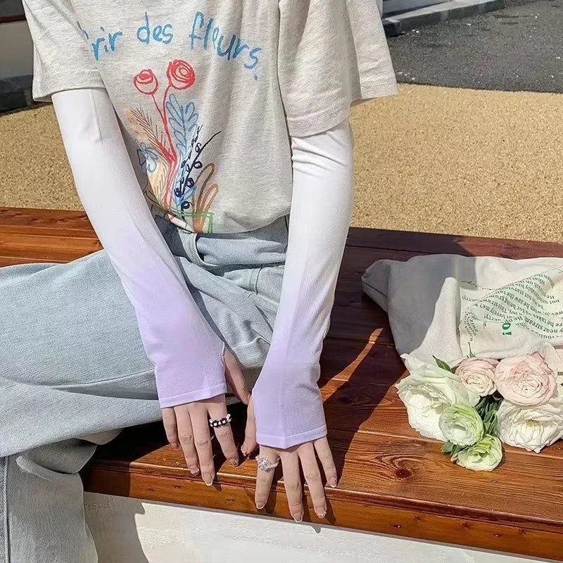 Person in light grey outfit wearing long gradient arm sleeves, sitting on bench with tote bag and pastel flowers