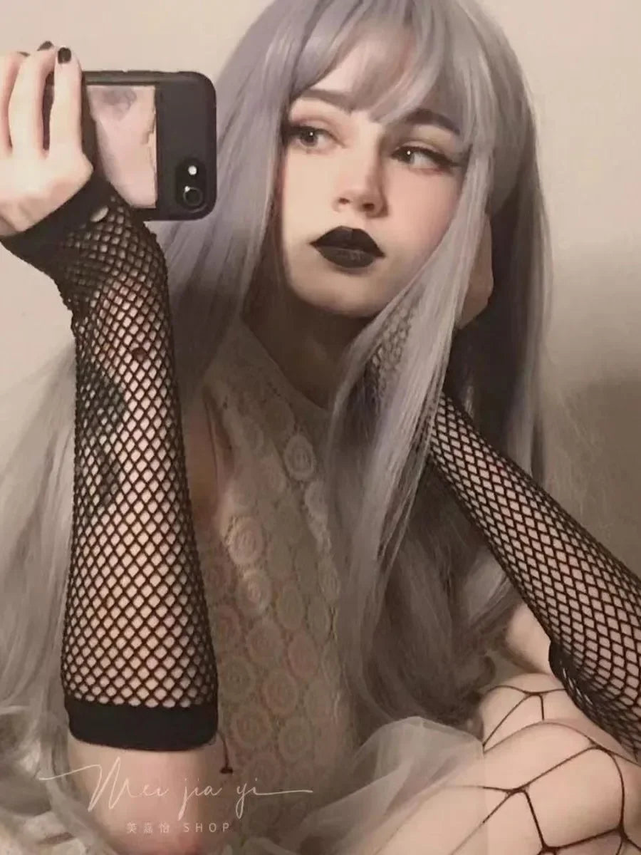 Woman with long silver hair, black lipstick, and black fishnet arm sleeves taking a selfie