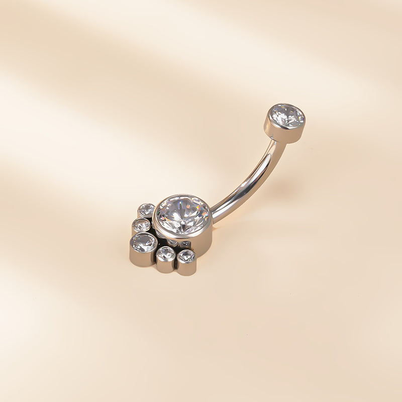 Curved silver belly button ring with clear round crystals on a beige background