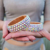 Hands holding two sparkling rhinestone-studded bangle bracelets, iridescent fashion accessories