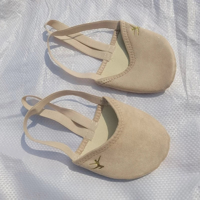Pair of beige suede dance shoes with elastic straps on a white textured surface