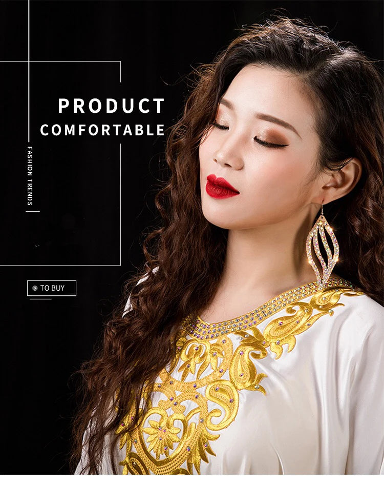 Woman with long wavy hair wearing gold embroidered white dress and statement earrings