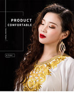 Woman with long wavy hair wearing gold embroidered white dress and statement earrings