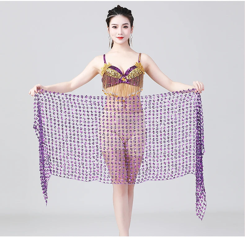 Woman in gold and purple belly dance costume holding a purple sequin shawl, studio background